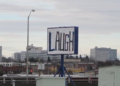 A commandeered sign on the side of the freeway hand painted with the word Laugh in all caps