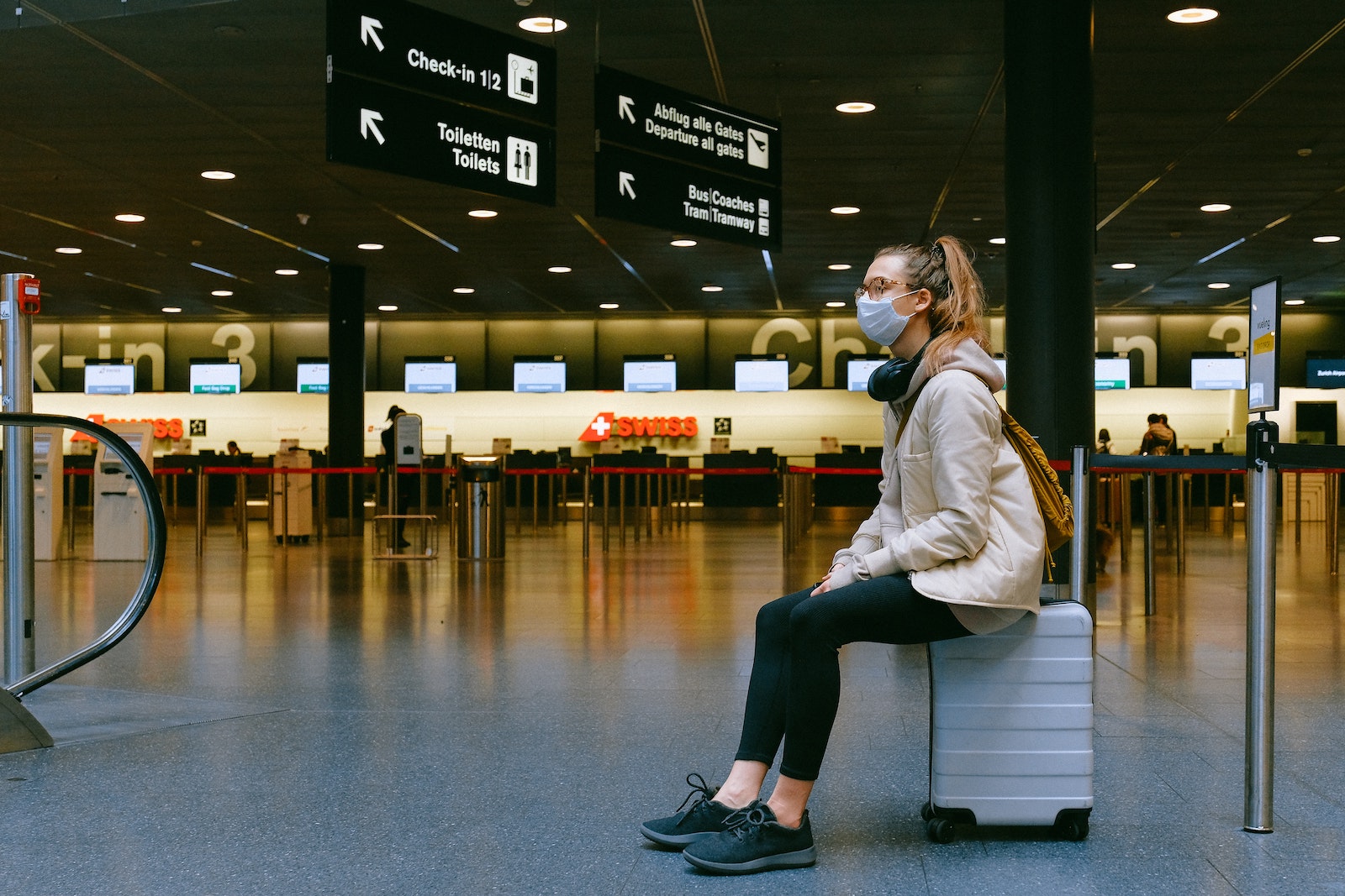 woman sitting on luggage wearing a mask in an airport