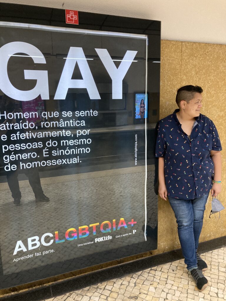 Maylene standing beside a metro advertisement being LGBTQ in Portugal