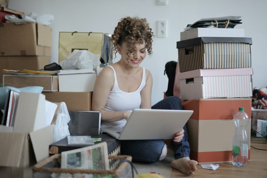 Woman sits amongst a pile of boxes filled with mail while looking at her laptop and smiling because a virtual mailbox has simplified her life