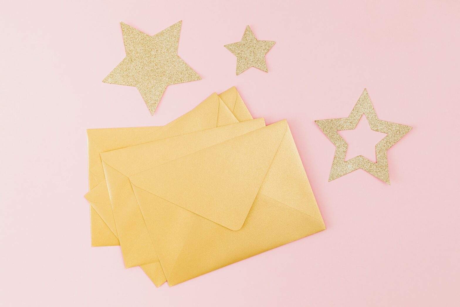 Gold stars surround a stack of gold envelopes against a pink background