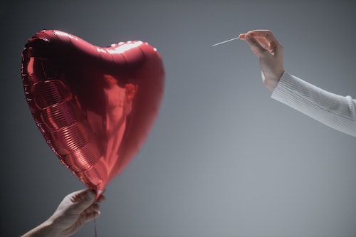 Person popping a heart-shaped balloon with a sharp object